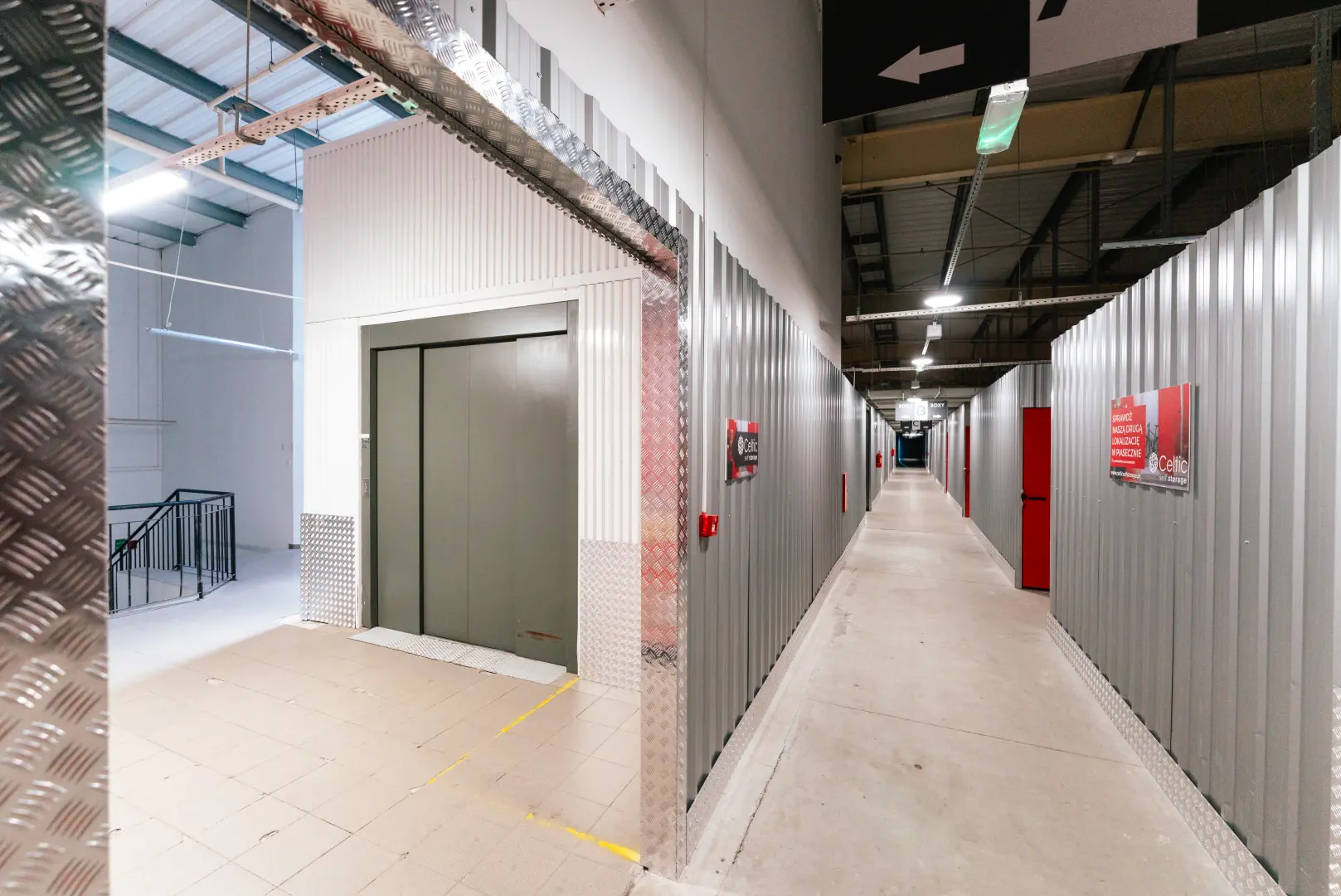 Korytarz magazynowy Celtic Self Storage — winda towarowa i boksy z czerwonymi drzwiami