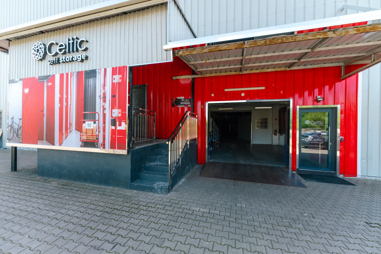 Wejście do magazynu Celtic Self Storage Łomianki — czerwona fasada z bramą wjazdową
