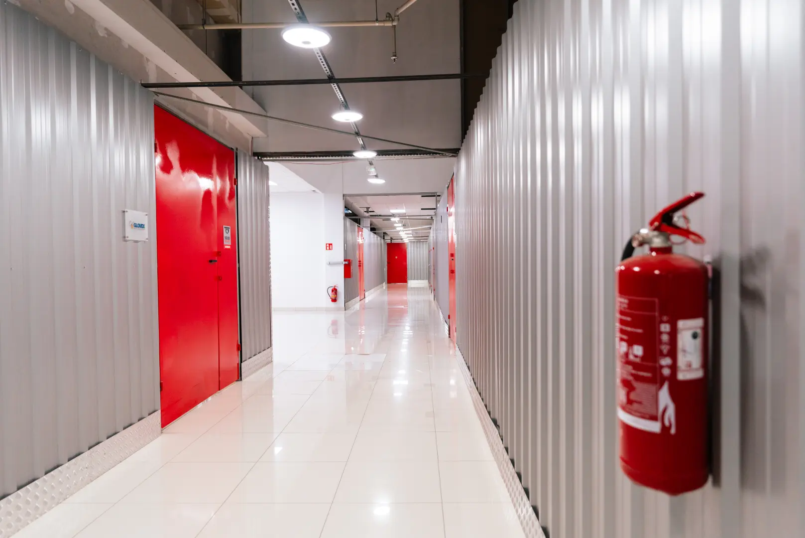 Czysty korytarz magazynowy Celtic Self Storage Łomianki z gaśnicą i czerwonymi drzwiami boksów