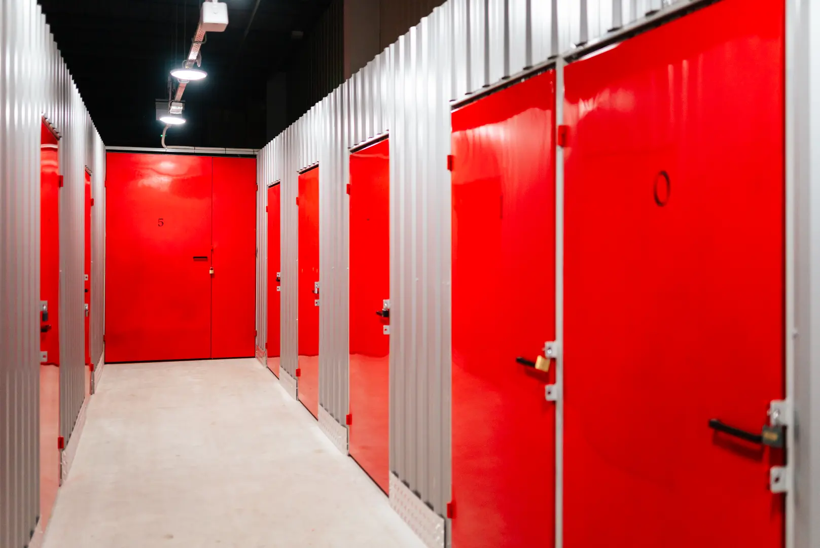 Korytarz boksów magazynowych z kłódkami i czerwonymi drzwiami w Celtic Self Storage Łomianki